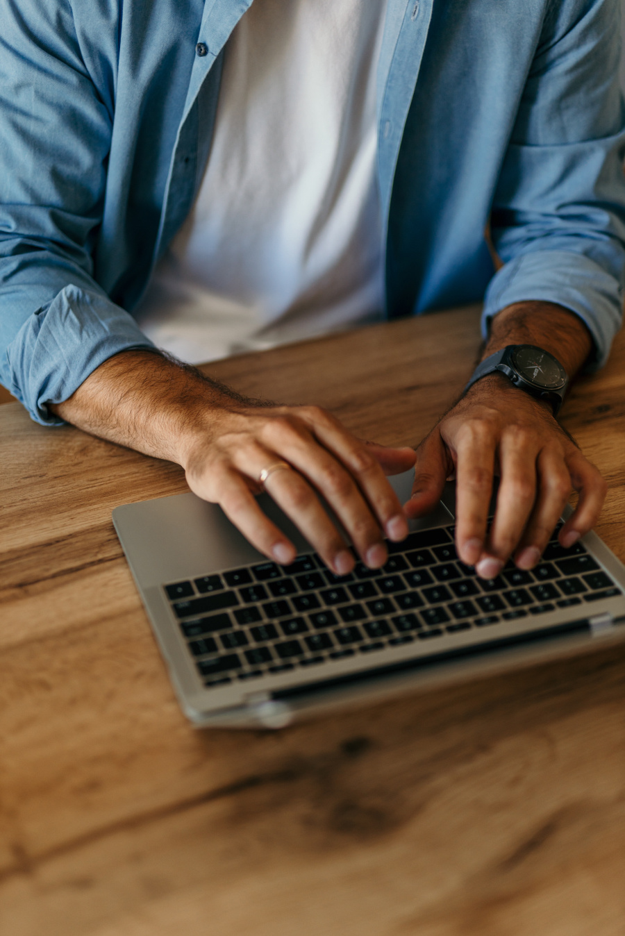 Male hands typing on a laptop keyboard while working from home